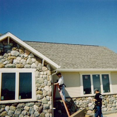 Two men repairing the gutter on the side of a home