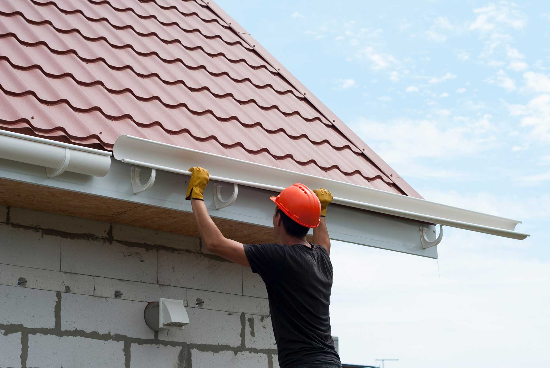 Man in orange hardhat installing gutters on new construction