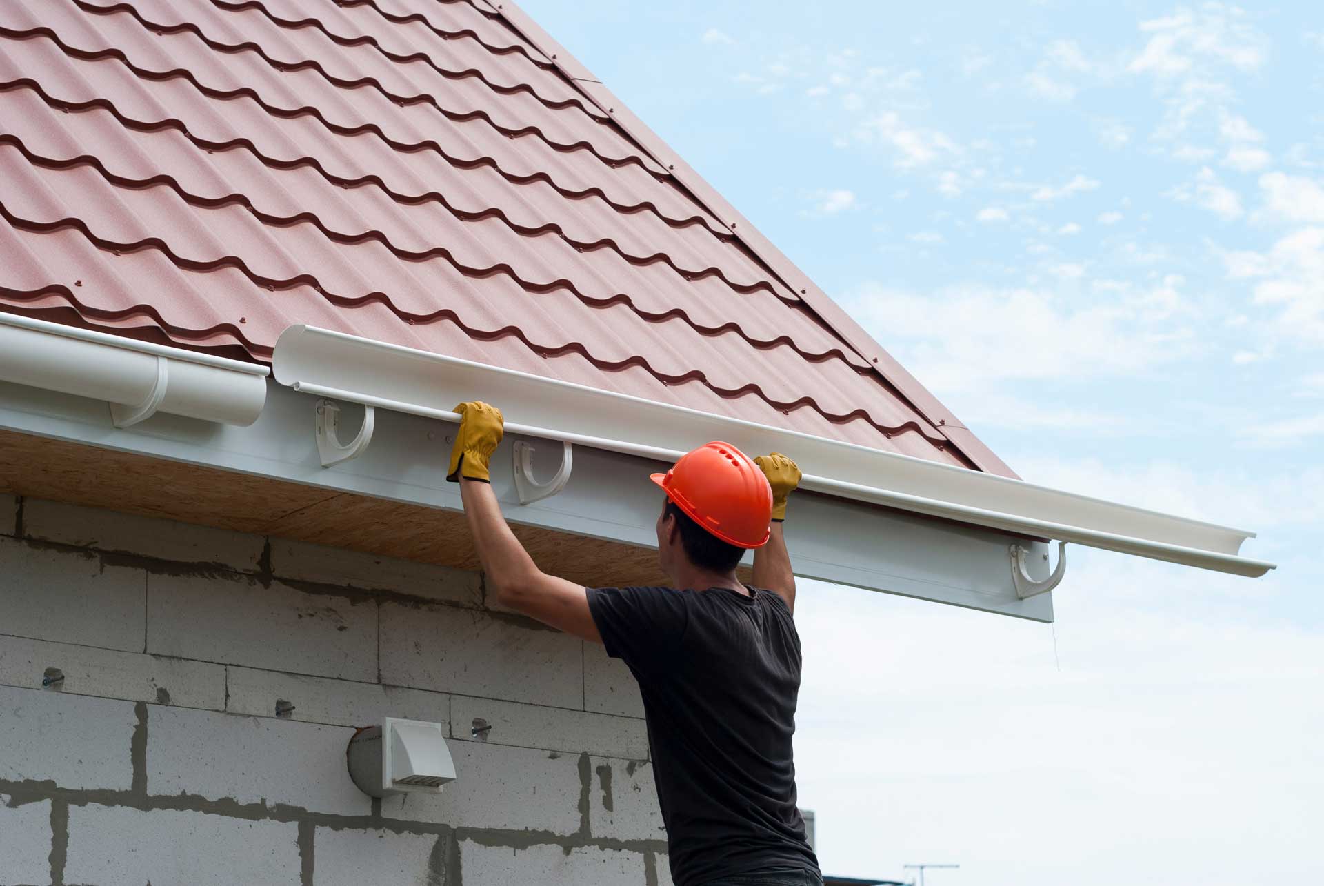 Man in orange hardhart installing gutters on new construction