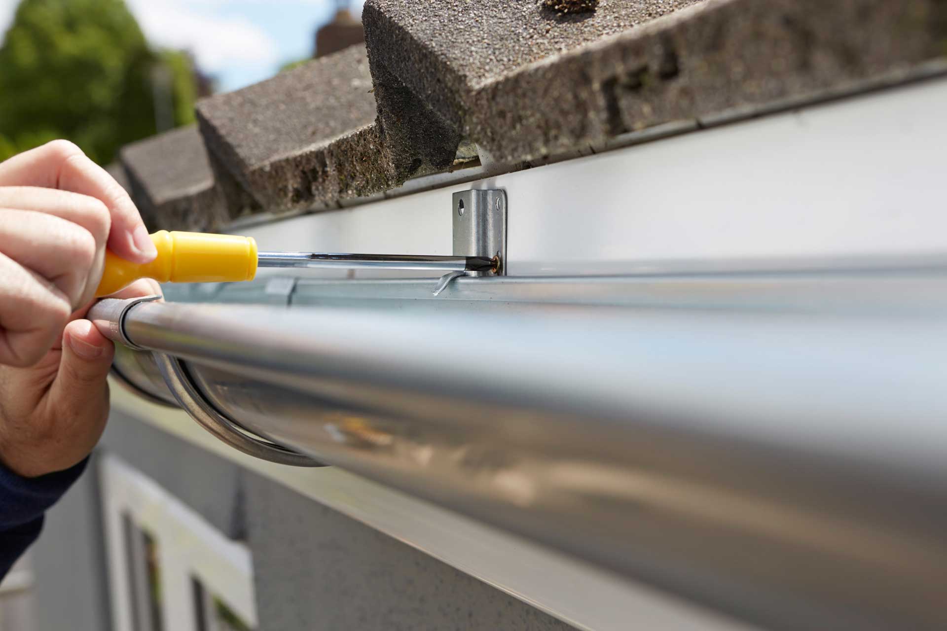 Close up of hands fastening new aluminum gutters on to home with yellow screwdriver